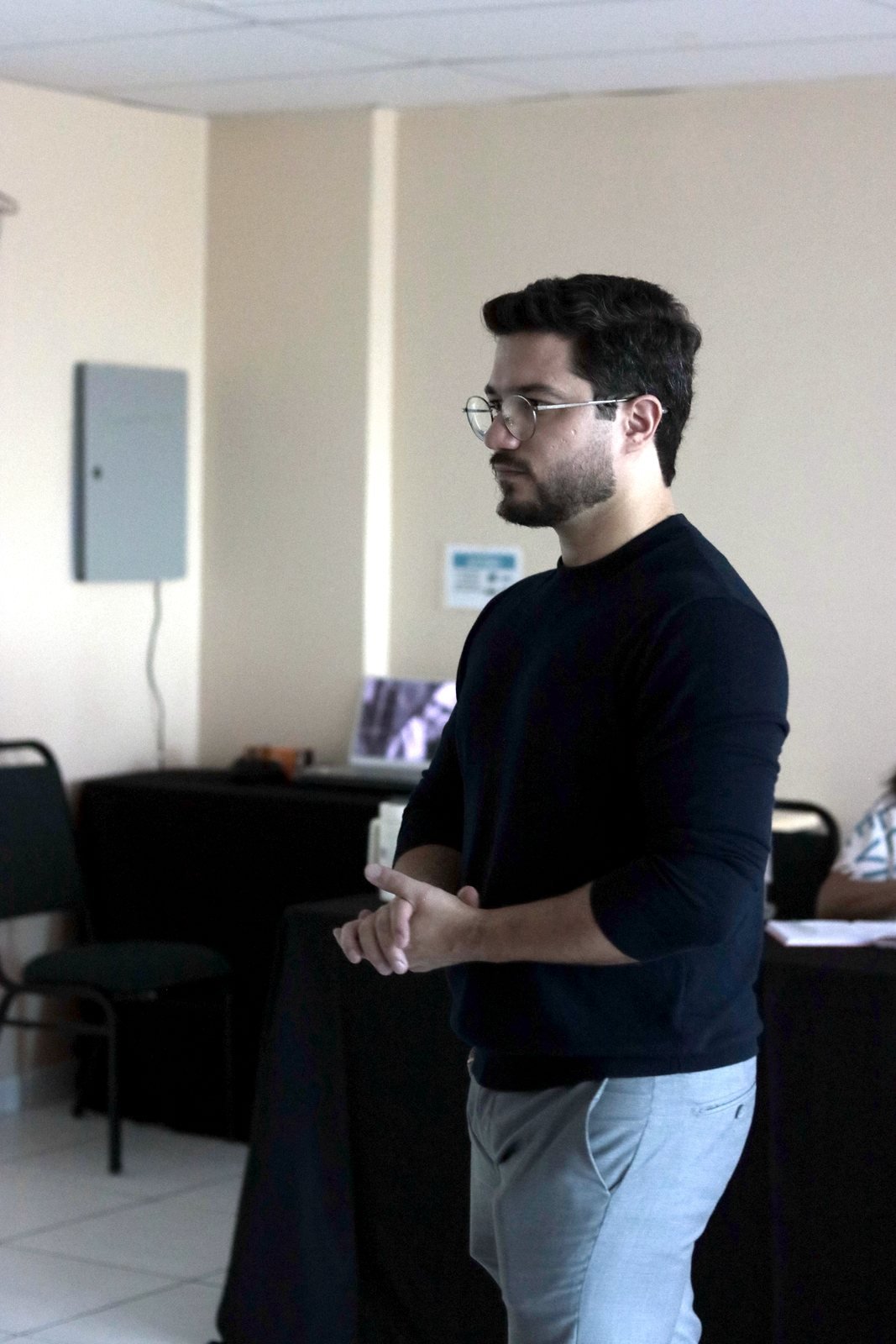 Caio Benevides em pé na sala, de frente para os participantes